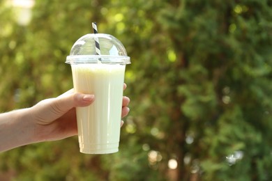 Photo of Woman holding tasty milkshake in plastic cup outdoors, closeup. Space for text