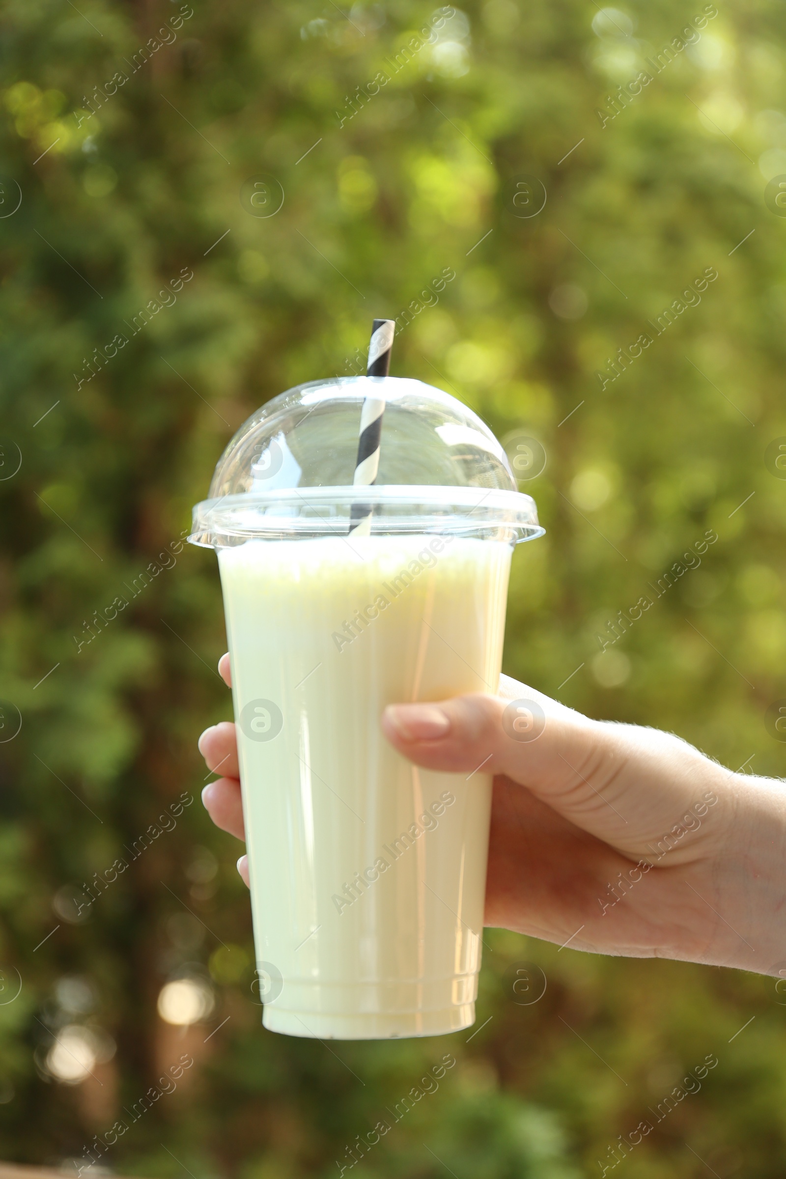 Woman holding tasty milkshake in plastic cup outdoors, closeup Photo of Woman holding tasty milkshake in plastic cup outdoors, closeup