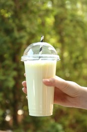 Photo of Woman holding tasty milkshake in plastic cup outdoors, closeup
