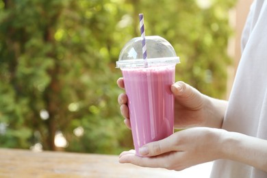 Photo of Woman holding tasty milkshake in plastic cup outdoors, closeup
