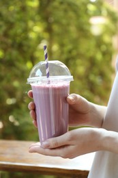 Photo of Woman holding tasty milkshake in plastic cup outdoors, closeup