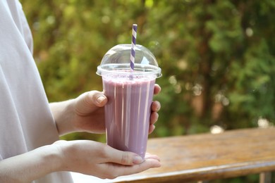 Photo of Woman holding tasty milkshake in plastic cup outdoors, closeup. Space for text