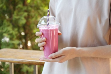 Photo of Woman holding tasty milkshake in plastic cup outdoors, closeup