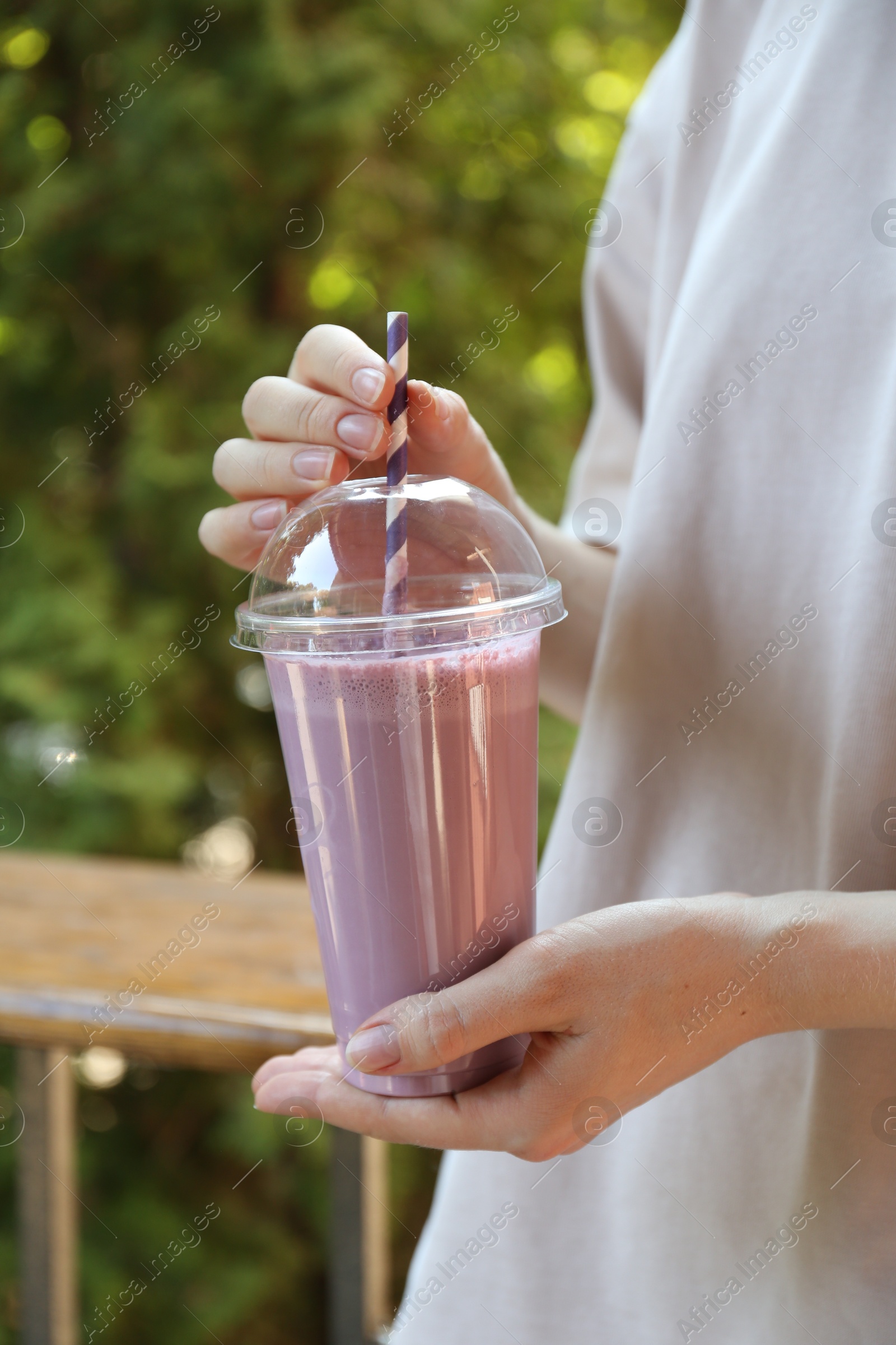 Woman holding tasty milkshake in plastic cup outdoors, closeup Photo of Woman holding tasty milkshake in plastic cup outdoors, closeup