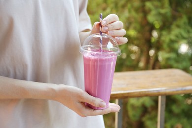 Photo of Woman holding tasty milkshake in plastic cup outdoors, closeup