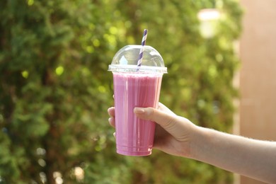 Photo of Woman holding tasty milkshake in plastic cup outdoors, closeup