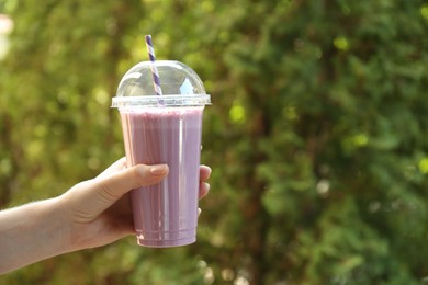 Photo of Woman holding tasty milkshake in plastic cup outdoors, closeup. Space for text