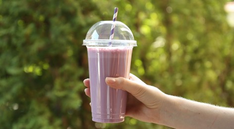 Photo of Woman holding tasty milkshake in plastic cup outdoors, closeup