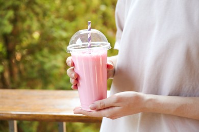 Photo of Woman holding tasty milkshake in plastic cup outdoors, closeup