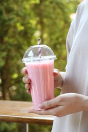 Photo of Woman holding tasty milkshake in plastic cup outdoors, closeup