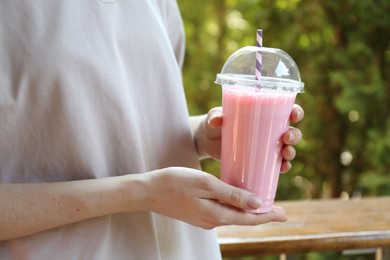 Photo of Woman holding tasty milkshake in plastic cup outdoors, closeup