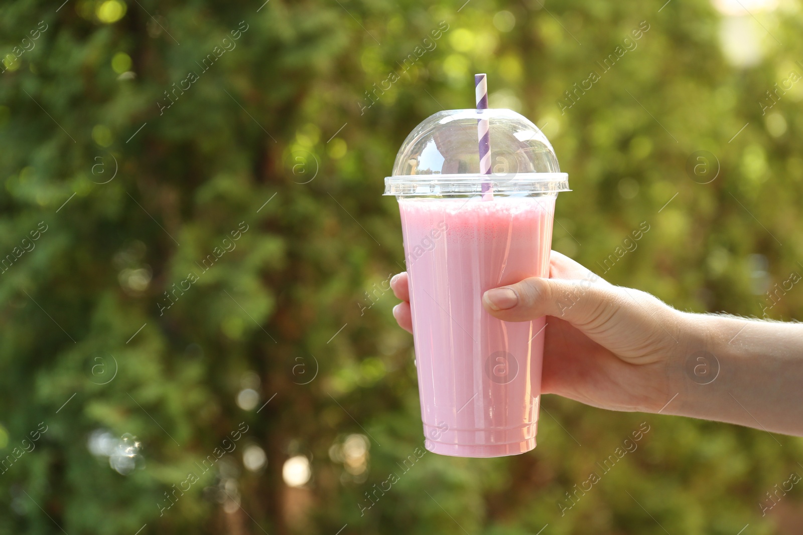 Photo of Woman holding tasty milkshake in plastic cup outdoors, closeup. Space for text