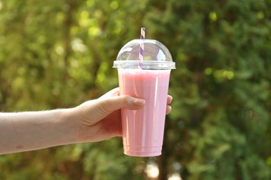 Photo of Woman holding tasty milkshake in plastic cup outdoors, closeup