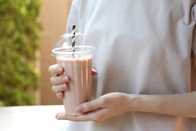 Photo of Woman holding tasty milkshake in plastic cup outdoors, closeup