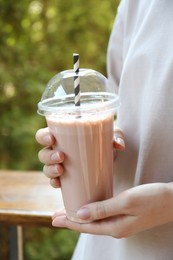 Photo of Woman holding tasty milkshake in plastic cup outdoors, closeup