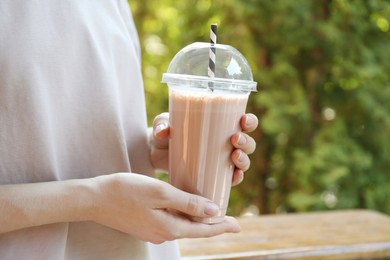 Photo of Woman holding tasty milkshake in plastic cup outdoors, closeup