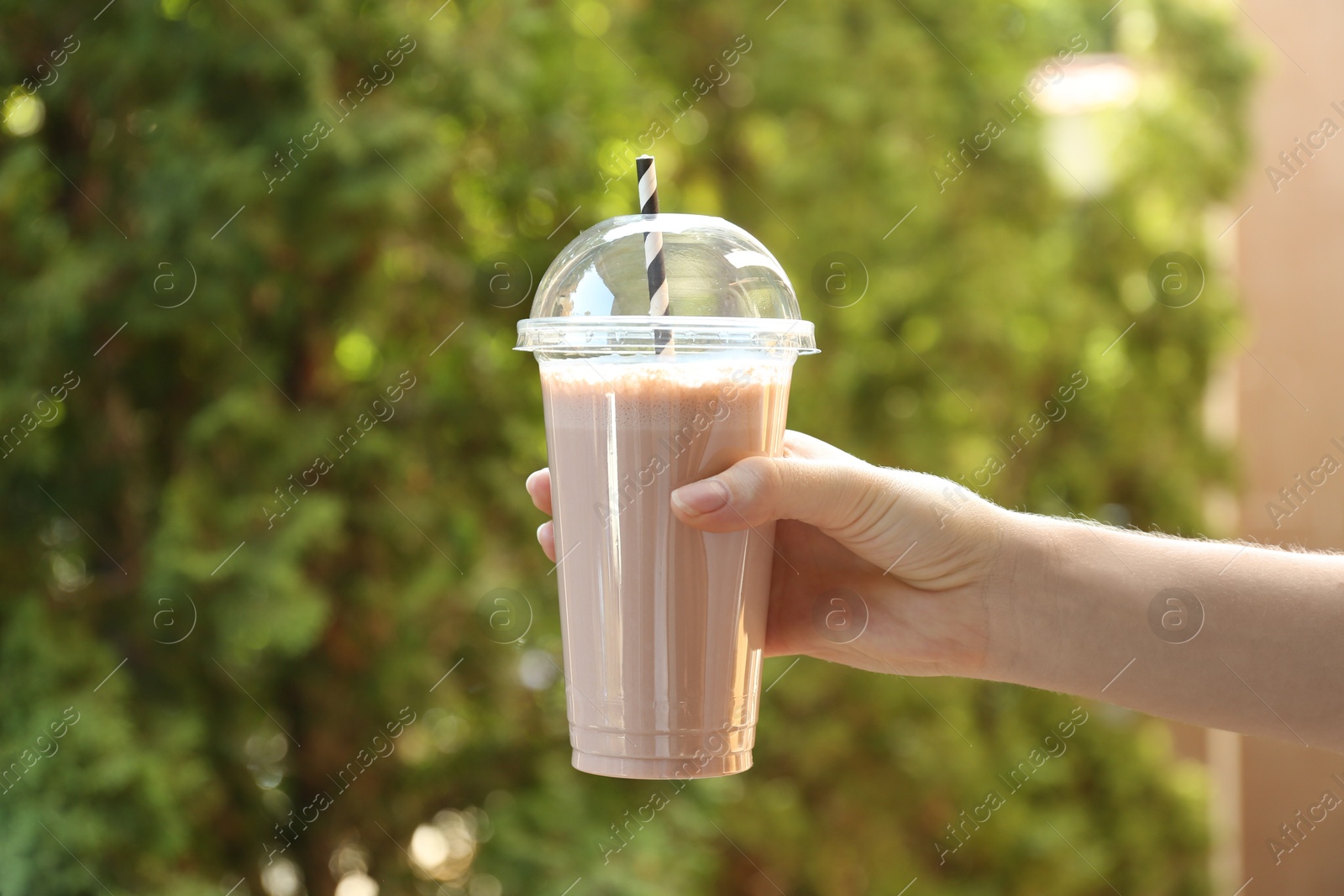 Woman holding tasty milkshake in plastic cup outdoors, closeup Photo of Woman holding tasty milkshake in plastic cup outdoors, closeup
