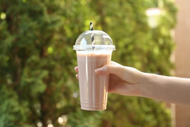 Photo of Woman holding tasty milkshake in plastic cup outdoors, closeup