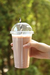 Photo of Woman holding tasty milkshake in plastic cup outdoors, closeup