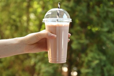 Photo of Woman holding tasty milkshake in plastic cup outdoors, closeup