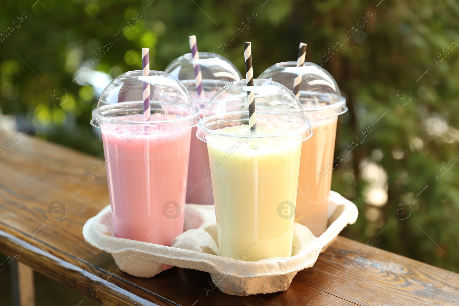 Tasty milkshakes in plastic cups on wooden table outdoors Photo of Tasty milkshakes in plastic cups on wooden table outdoors