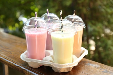Photo of Tasty milkshakes in plastic cups on wooden table outdoors