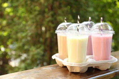 Photo of Tasty milkshakes in plastic cups on wooden table outdoors