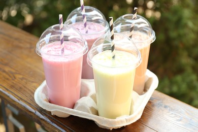 Photo of Tasty milkshakes in plastic cups on wooden table outdoors, closeup