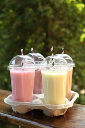 Photo of Tasty milkshakes in plastic cups on wooden table outdoors