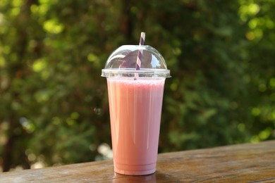 Photo of Tasty milkshake in plastic cup on wooden table outdoors