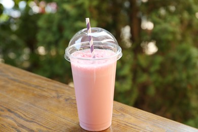 Photo of Tasty milkshake in plastic cup on wooden table outdoors