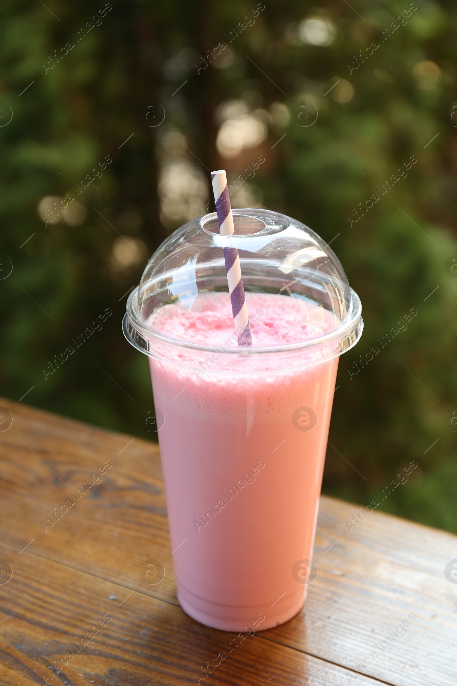 Tasty milkshake in plastic cup on wooden table outdoors Photo of Tasty milkshake in plastic cup on wooden table outdoors