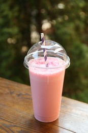 Photo of Tasty milkshake in plastic cup on wooden table outdoors