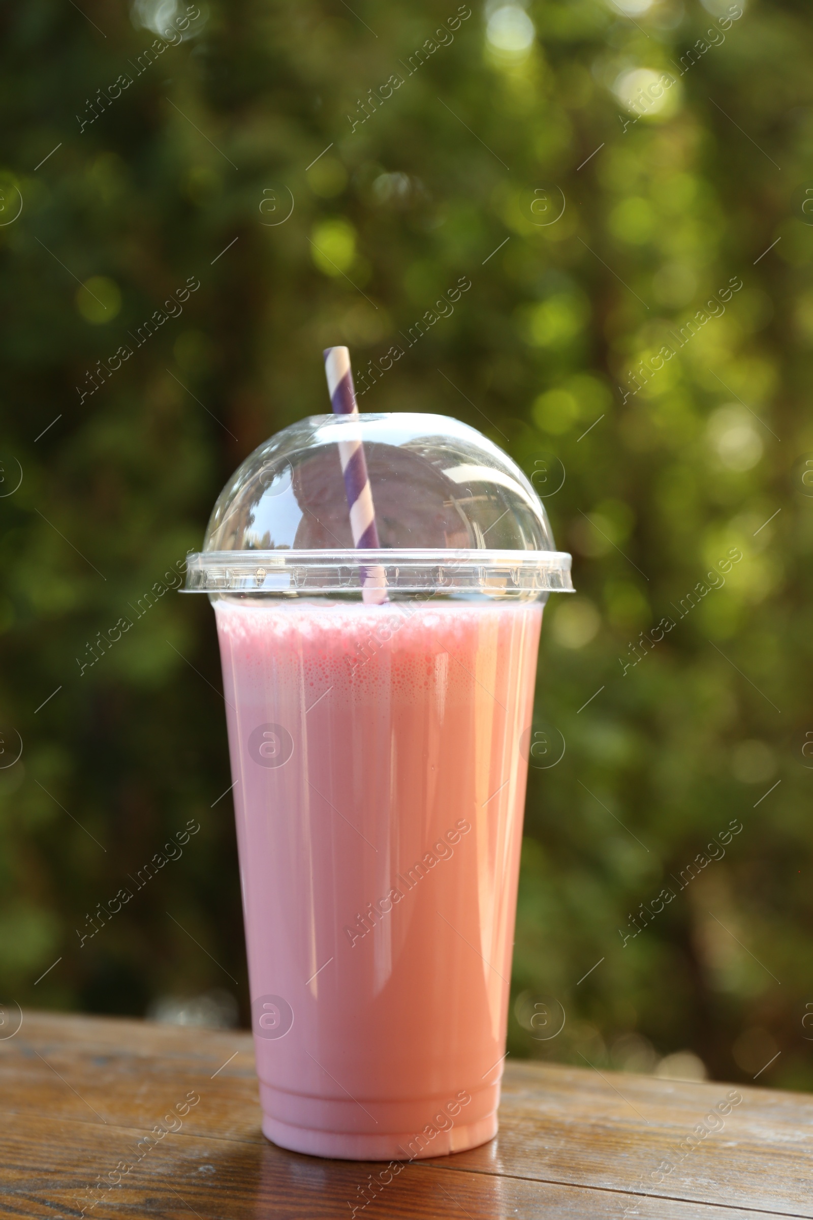 Tasty milkshake in plastic cup on wooden table outdoors Photo of Tasty milkshake in plastic cup on wooden table outdoors