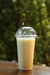 Photo of Tasty milkshake in plastic cup on wooden table outdoors
