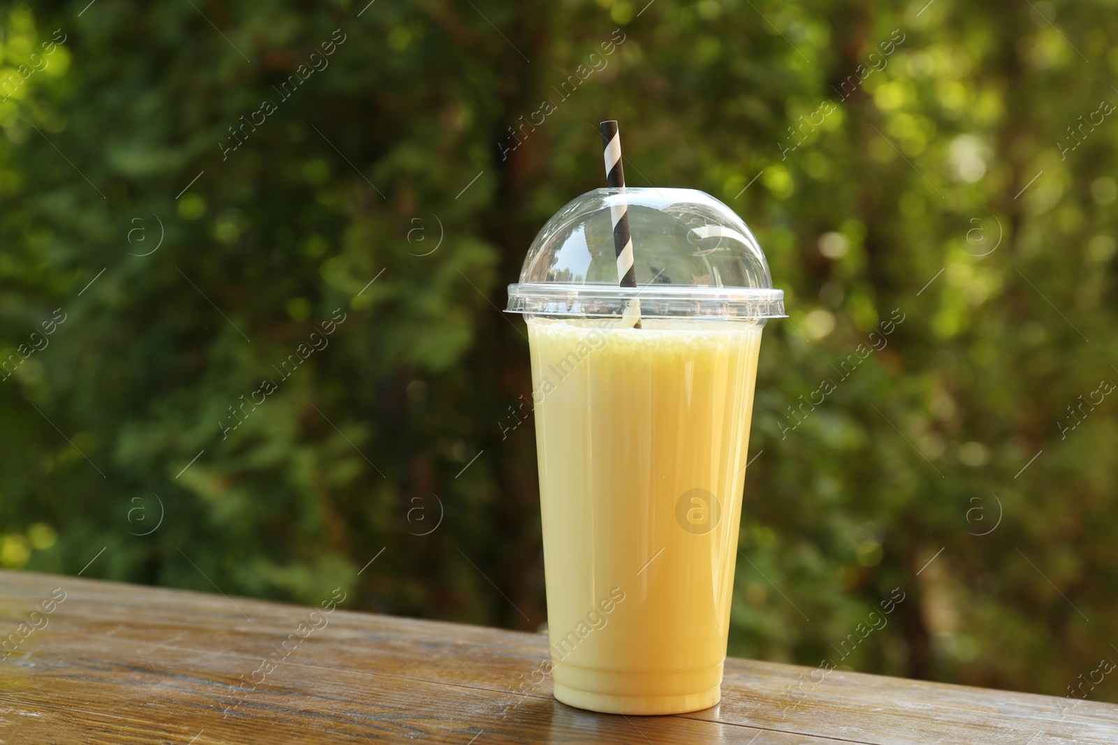 Tasty milkshake in plastic cup on wooden table outdoors Photo of Tasty milkshake in plastic cup on wooden table outdoors