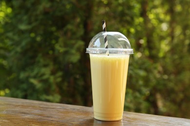 Photo of Tasty milkshake in plastic cup on wooden table outdoors
