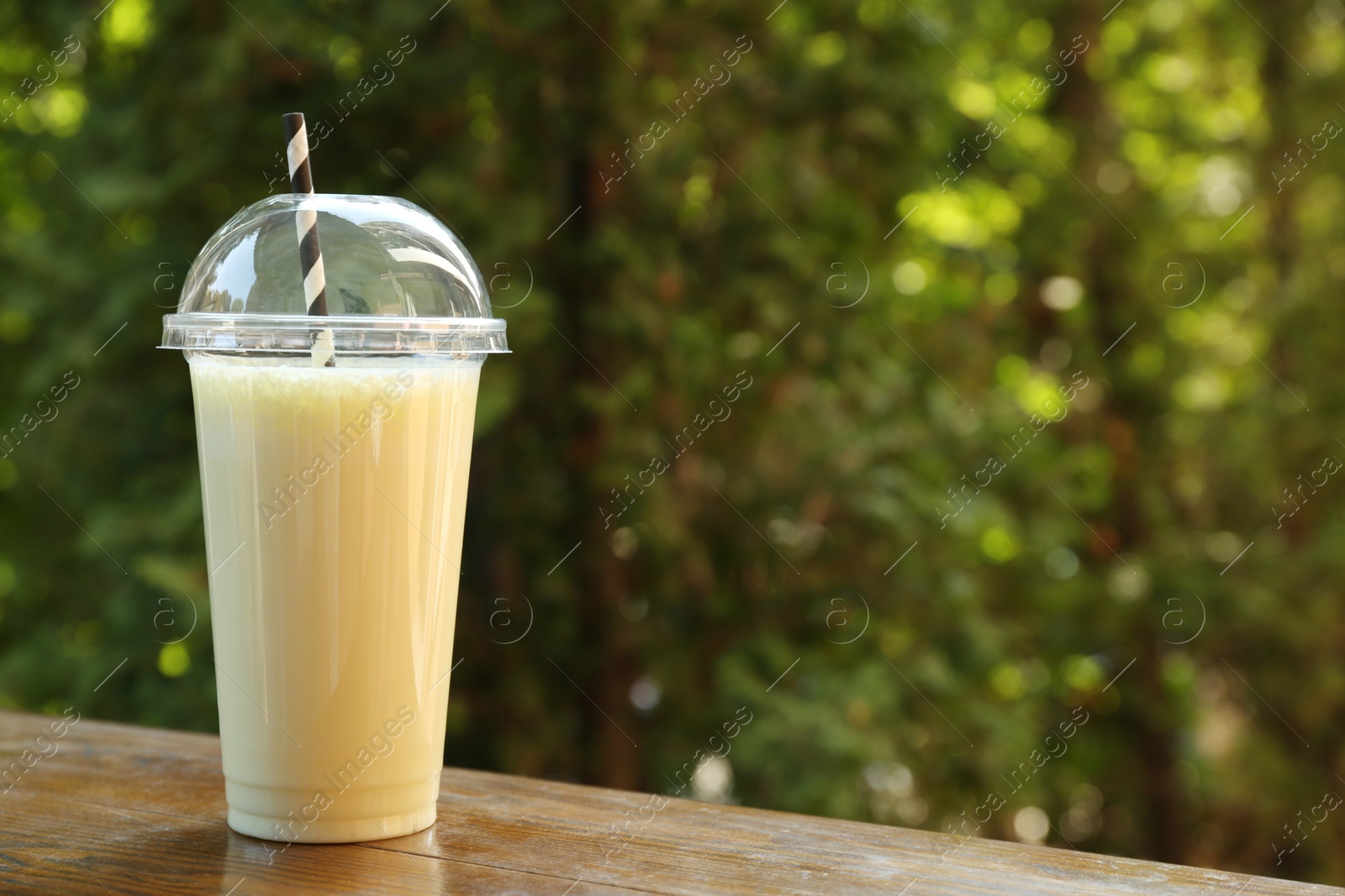 Tasty milkshake in plastic cup on wooden table outdoors, space for text Photo of Tasty milkshake in plastic cup on wooden table outdoors, space for text