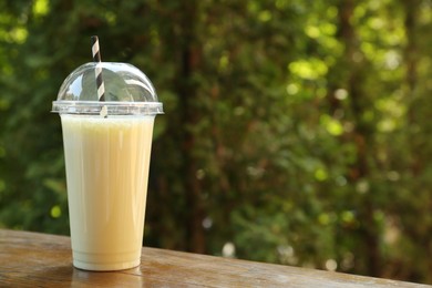 Photo of Tasty milkshake in plastic cup on wooden table outdoors, space for text