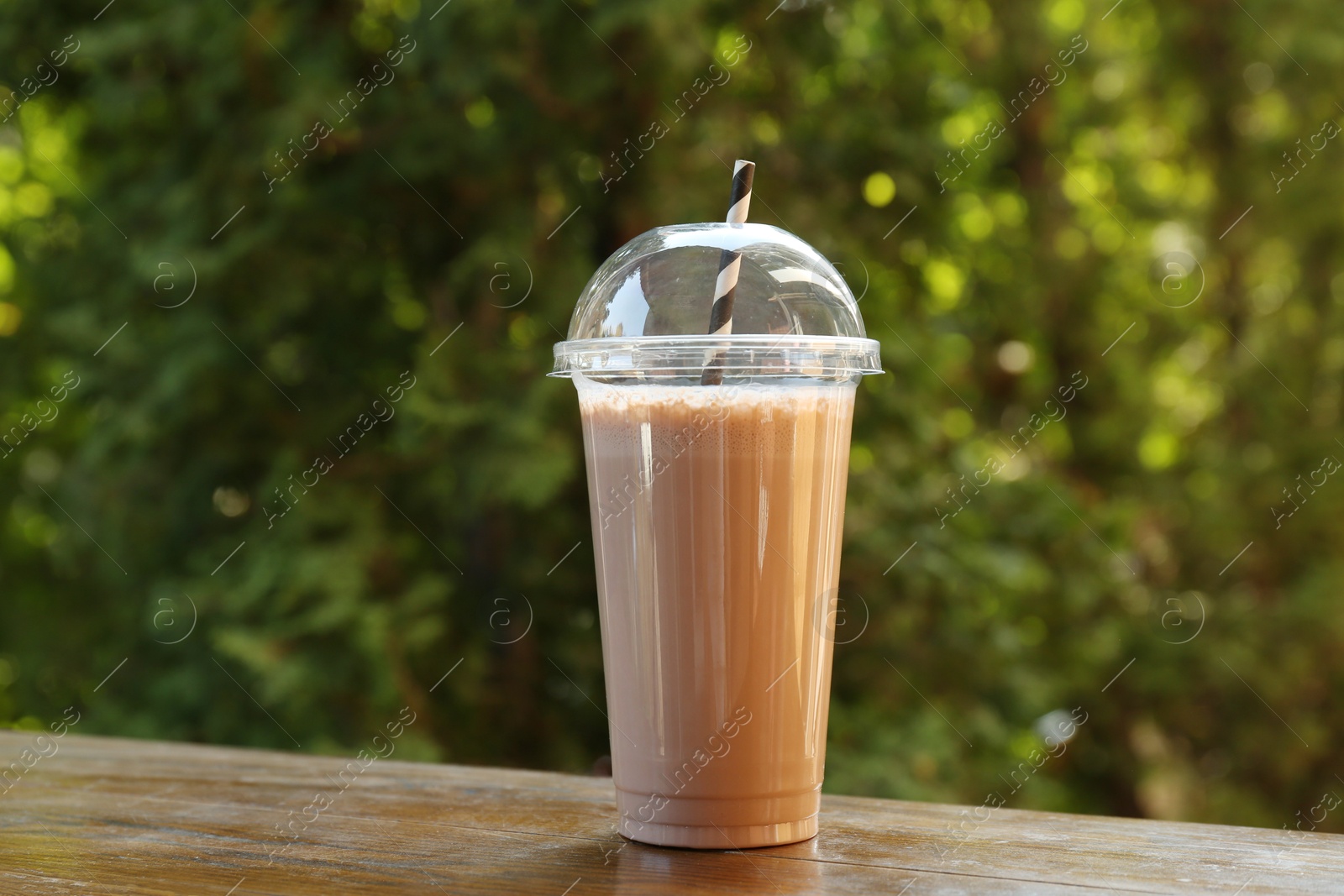 Photo of Tasty milkshake in plastic cup on wooden table outdoors