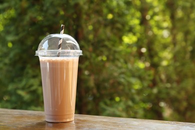 Photo of Tasty milkshake in plastic cup on wooden table outdoors, space for text