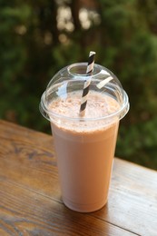 Photo of Tasty milkshake in plastic cup on wooden table outdoors