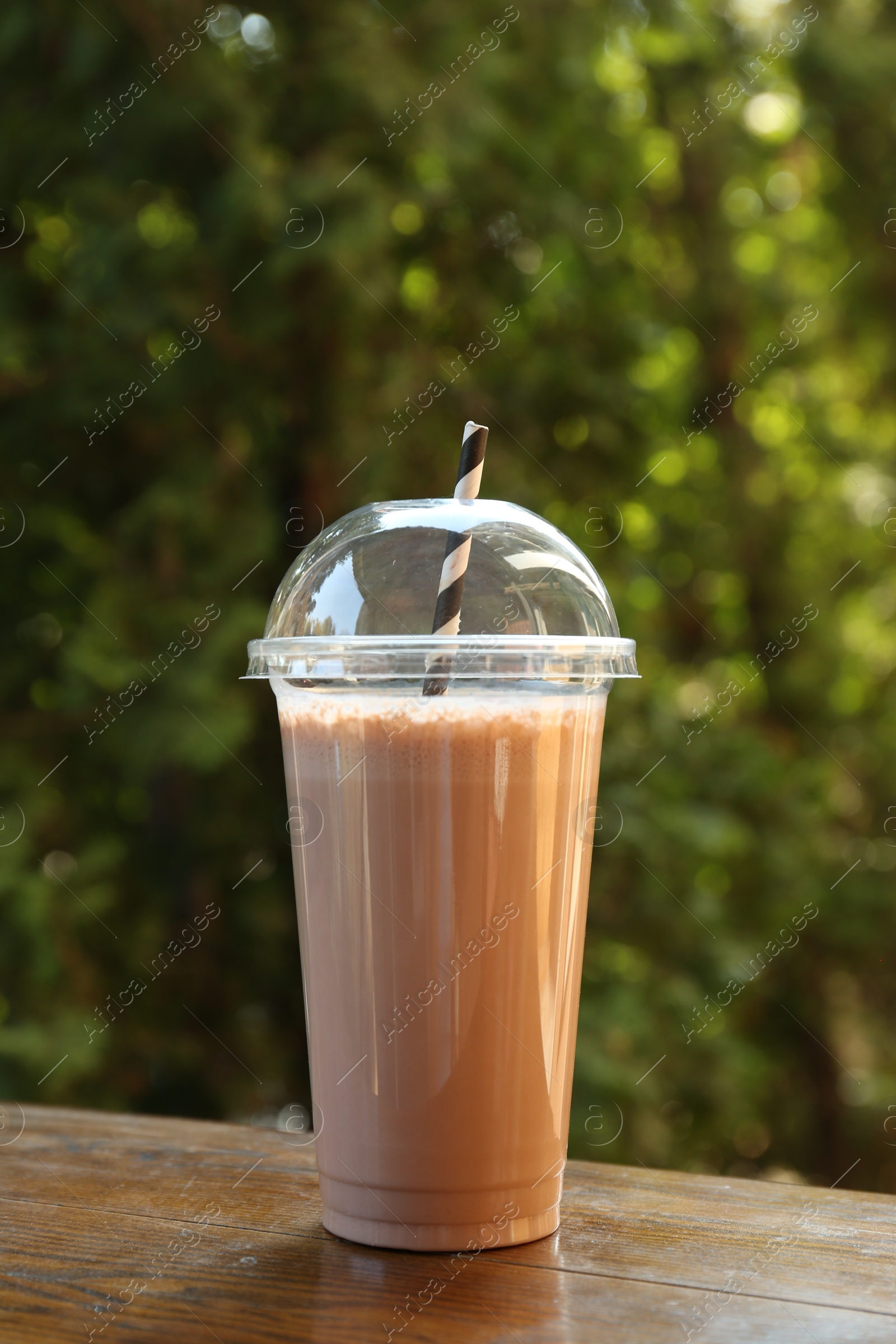 Photo of Tasty milkshake in plastic cup on wooden table outdoors