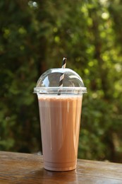 Photo of Tasty milkshake in plastic cup on wooden table outdoors