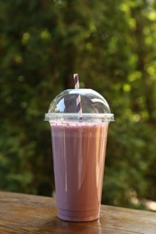 Photo of Tasty milkshake in plastic cup on wooden table outdoors