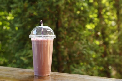 Photo of Tasty milkshake in plastic cup on wooden table outdoors , space for text