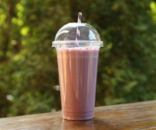 Photo of Tasty milkshake in plastic cup on wooden table outdoors