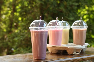 Photo of Tasty milkshakes in plastic cups on wooden table outdoors