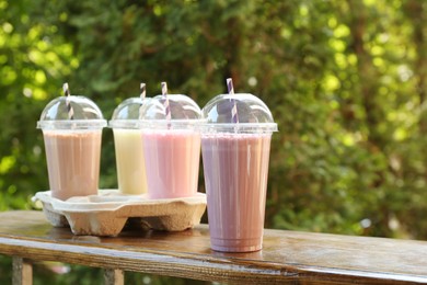 Photo of Tasty milkshakes in plastic cups on wooden table outdoors, space for text