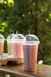 Photo of Tasty milkshakes in plastic cups on wooden table outdoors